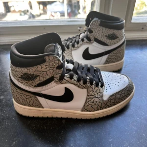 Jordan 1 High ”White cement” - Säljer ett par Nike Air Jordan 1 High med ikoniskt elephant print i grått och svart, vita paneler och svarta detaljer. Skorna har svart swoosh, svarta skosnören och klassisk hög siluett. Ovandelen är i skinn och mönstret ger en riktigt unik vibe. Vita snören medföljes även.