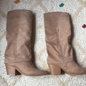 Beige mockastövlar med klack - Snygga och supersköna beigea knähöga stövlar i mocka-aktigt material med spetsig tå och stabil klack. Säljes på grund av att de är för stora, därmed använda fåtal gånger. Nypris 1000 kr. Klackhöjd 6 cm🤍 Ena stövelns söm har gått av lite på insidan, dock inget som inte går att sy ihop. 