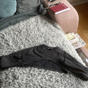 Grå croppad sweatshirt från Primark  - Säljer en svart croppad sweatshirt från Primark i storlek S. Tröjan har lång ärm, rund halsringning och är tillverkad i mjuk bomullsmix. Perfekt för lager-på-lager och ger en cool streetstyle-vibe till outfiten. 