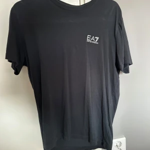 Mörkblå EA7 Emporio Armani t-shirt - Mörkblå t-shirt från EA7 Emporio Armani med diskret logga i vitt på bröstet. Klassisk rund hals och korta ärmar. Tillverkad i mjuk bomull som känns skön mot huden. Perfekt för en clean och stilren look.