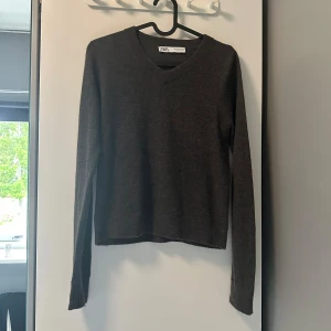 Mörkgrå stickad tröja från Zara - Mörkgrå stickad tröja från Zara med v-ringad hals och lång ärm. Enkel och stilren modell som är perfekt för lager-på-lager. Mjuk känsla och normal passform, passar till allt i garderoben.