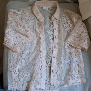 Beige spetsblus från Vila - Superfin beige spetsblus från Vila med korta ärmar och klassisk krage. Storlek 36. Blusen har blommigt spetsmönster och knäpps framtill med tygklädda knappar. Ganska kort, slutar vid midjan. Genomskinlig så jag har den med ett linne under. Perfekt för dig som vill ha en romantisk och luftig look. 