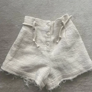 Vita högmidjade shorts från Zara - Snygga vita högmidjade shorts från Zara i grovvävd bomullsmix. De har knappar framtill, snörning i midjan och råa kanter nertill för en chill vibe. Perfekta för varma dagar när du vill ha något både bekvämt och trendigt.