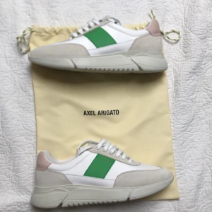 Axel Arigato sneakers med grön detalj - OBS! Priset är diskuterbart…                             Snygga sneakers från Axel Arigato i vitt med beige mockadetaljer och en grön panel på sidan. OBS! HELT NYA storlek 44, nypris 2500kr. Påsen ingår också i priset