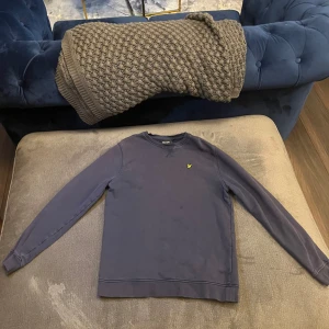 Marinblå crew neck sweatshirt från Lyle & Scott - Säljer en stilren marinblå sweatshirt från Lyle & Scott med klassisk rund hals och det ikoniska gula logobroderiet på bröstet. Tröjan har långa ärmar och är gjord i mjuk bomull, perfekt för en chill och snygg look.. Har en eller två fläckar men är i ganska bra skick