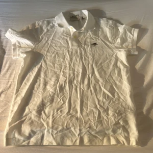 Vit pikétröja från GANT, stl S - Klassisk vit pikétröja från GANT i regular fit. Tröjan har korta ärmar, krage och knäppning framtill samt en liten broderad logga på bröstet. Perfekt till jeans eller shorts för en clean och stilren look.