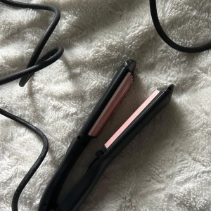 Svart våffeltång från BaByliss Paris - Säljer en svart plattång från BaByliss Paris med rosafärgad innersida. Perfekt för att styla håret vågigt. Sladden är lång och flexibel, och designen är smidig att använda. Passar dig som vill ha ett snyggt och stylat hår snabbt.