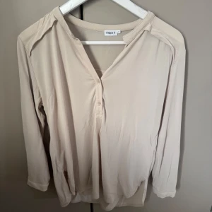 Beige blus från Filippa K smal - Snygg beige blus från Filippa K med v-ringning och knappar framtill. Lätt och mjukt material som känns skönt mot huden. Perfekt med trekvartsärm och stilren design som passar till många olika looks.