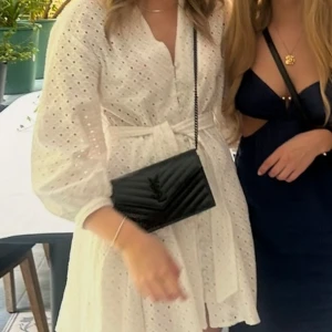 Vit kort klänning från Zara med band - Superfin vit kort klänning från Zara med broderade hål, knappar framtill och knytband i midjan. Har bara använt den en gång så den är som ny. Perfekt för midsommar eller som vardagsklänning i sommar!