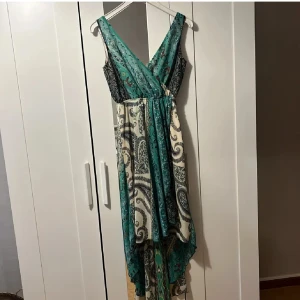 Blommig långklänning från Dry Lake - Superfin långklänning från Dry Lake med blommigt mönster i turkos, beige och svart. Omlottmodell med v-ringning och ärmlös design.  Helt ny prislappen kvar. Strl XS men passar även S.
