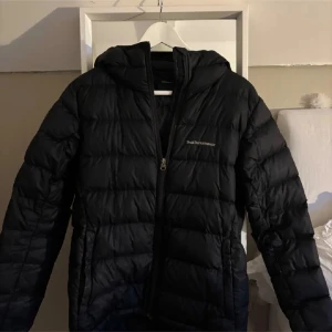 Svart dunjacka Peak Performance - Svart dunjacka från Peak Performance med luva och dragkedja. Jackan har några defekter (se bild 2 och 3) köparen står för frakt! pris går att diskutera!