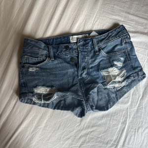 Blå slitna jeansshorts Abercrombie - Snygga blå jeansshorts från Abercrombie & Fitch med slitna detaljer och råa kanter. Klassisk femficksmodell med låg midja och knappar framtill. Perfekta för sommaren och ger en avslappnad vibe. Tidlös denim som alltid funkar. Skriv om ni undrar något💕