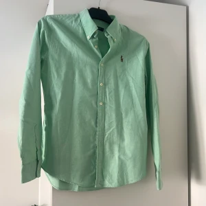 Mintgrön skjorta från Ralph Lauren - Snygg mintgrön skjorta från Ralph Lauren i slim fit-modell. Skjortan har klassisk krage, långa ärmar och knäppning framtill. Ikoniska broderade loggan på bröstet. Perfekt för dig som gillar stilrena och fräscha plagg.