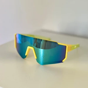 Sportiga barn solglasögon  - Futuristiska solglasögon för barn med stora blågröna spegelglas och cool gul ram. Sköldformad design som täcker mycket av ansiktet och ger en riktigt sportig vibe😎Perfekta för dig som vill sticka ut och gillar färg. Lätta och bekväma att bära💪