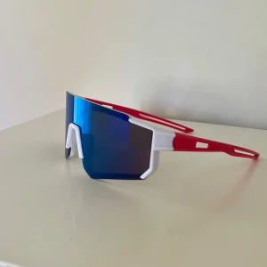 Sportiga barn solglasögon - Säljer ett par riktigt sportiga barnsolglasögon med spegelblått visir och cool båge i vitt och rött. De har en futuristisk, kantig form och bred lins som täcker bra😎 Perfekta för dig som vill sticka ut på träningen eller cykelturen💪
