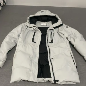 Vit dunjacka från Sail Racing, M - Säljer en snygg vit dunjacka från Sail Racing ÄKTA! I storlek medium. Jackan har svart foder, huva och flera dragkedjeförsedda fickor framtill. Yttermaterialet är polyester med lite spandex för extra rörlighet och fyllningen består av certifierat ankdun och fjäder.
