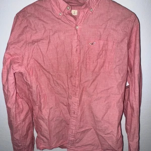 Rosa skjorta från Hollister, stl S - Snygg rosa skjorta från Hollister med klassisk button-down krage och bröstficka med broderad logga. Skjortan är långärmad och har knappar hela vägen framtill. Perfekt för dig som gillar en avslappnad men stilren look.