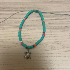 Turkost armband med sköldpaddshänge - Färgglatt armband med turkosa pärlor och inslag av rosa, vitt, orange och blått. Armbandet har ett justerbart band och ett silverfärgat hänge i form av en söt sköldpadda. Perfekt accessoar för dig som gillar strandvibbar och unika detaljer.