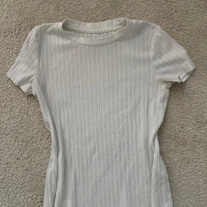 Vit ribbad kortklänning - En enkel och stilren vit ribbad kortklänning med rund hals och korta ärmar. Klänningen har en figurnära passform och är perfekt för en avslappnad look. Materialet känns mjukt och stretchigt.