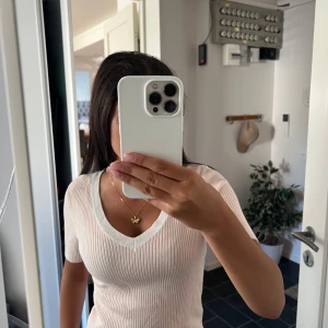 Ribbad vit topp från Divided - Säljer en ribbad, ljusvit topp från Divided med v-ringning och korta ärmar. Toppen har en slim passform och är tillverkad i mjuk bomullsmix. Perfekt till jeans eller kjol för en clean och fräsch look.