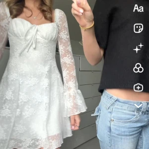 Vit spetsklänning med trumpetärm - Superfin vit kortklänning med blommigt spetsmönster och transparenta trumpetärmar. Söt knytning framtill och figurnära passform upptill, sedan utsvängd kjol. Perfekt för sommarens alla tillfällen!