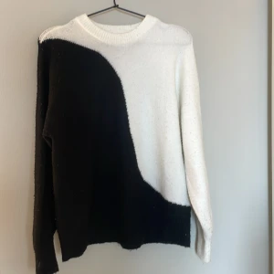 Svart/vit  stickad tröja från Vila - Säljer en snygg svart/vit stickad tröja från Vila i storlek S. Tröjan har ett coolt, böljande färgblocksmönster och rund halsringning. Den är långärmad och gjord i mjuk och skön att ha på sig. 