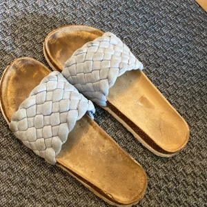 Ljusblå sandaler - Säljer ett par ganska slitna, ljusblå sandaler. Platt sula och öppen tå, med en bred, flätad rem i ljusblå. Gissningsvis i storlek 39.
