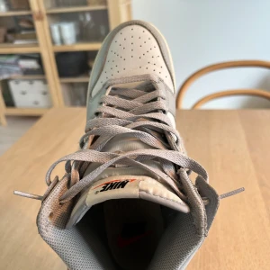 Nike Dunk High i grå mocka och skinn - Nike Dunk High sneakers i olika grå nyanser med ovandel i skinn och detaljer i mocka, inklusive en ullig Swoosh. Klassisk siluett med perforerad tå, grå snörning och gummisula. Retro Nike-logga på plösen. Perfekta för dig som gillar stilrena och unika sneakers. Kom privat för mer info 