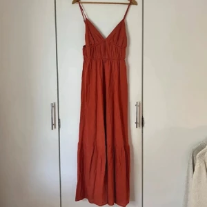 Rostfärgad långklänning med smala axelband - Säljer en snygg rostfärgad långklänning med smala axelband och v-ringning. Klänningen har markerad midja och faller luftigt ner till anklarna. Perfekt för varma dagar och har en enkel, stilren look. Står varken storlek eller märke men uppskattar den till en 38:a. Jag är 176cm 