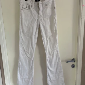 Vita bootcut jeans från True Religion - Storlek 27. Snygga vita jeans från True Religion i modellen Becca Mid Rise Bootcut. Jeansen har klassiska fem fickor, coola bakfickor med lock och silverfärgade knappar. Går bra att sy om till lågmidjade eller jeanskjol.