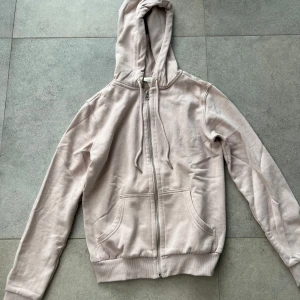 Ljusrosa hoodie med dragkedja H&M XS - Ljusrosa hoodie från H&M i storlek XS. Tröjan har dragkedja framtill, huva med snörning och två fickor. Tillverkad i mjuk bomullsmix, perfekt för chill dagar. Enkel och stilren design som funkar till det mesta.