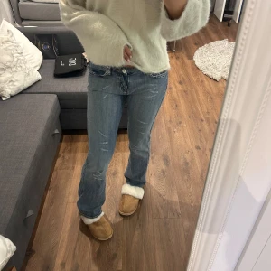 Blå bootcut jeans med slitningar - Snygga blå jeans med bootcut-modell och slitna detaljer framtill. Jeansen har låg midja och klassisk femficksdesign. Materialet är denim och passformen är normal med lätt utsvängda ben. Perfekta för en avslappnad och trendig look.