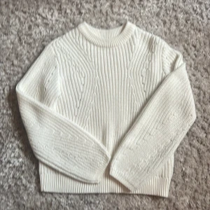 Vit stickad tröja med strukturmönster - Säljer en vit stickad tröja med snyggt strukturmönster och ribbade muddar. Tröjan har rund halsringning och långa ärmar, perfekt för lager på lager under kyliga höst och vinter dagar. Enkel att matcha med jeans eller kjol för en clean look.