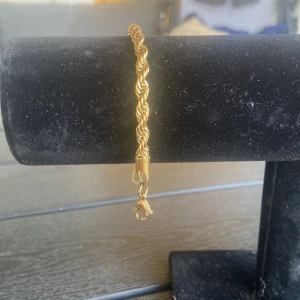 Guldigt tvinnat armband - Snyggt armband i guldig färg med tvinnad kedja och karbinlås. Armbandet är i nytt skick, armbandet är inte i riktigt guld men är gjord av stål, 17cm lång, 50kr