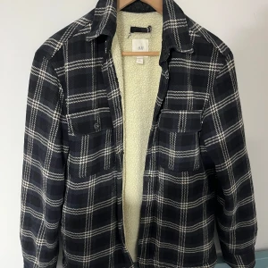 Rutig jacka från H&M, svart/vit - Snygg rutig teddyjacka från H&M i svart och vitt. Jackan har mjukt teddyfoder, klassisk krage och två bröstfickor med knappar. Perfekt för kyliga dagar och ger en avslappnad men trendig look. Öppen för bundles och frågor!  Man, kille, grisch, Stockholm, plagg, billigt, small, s, stil, stiligt, style, jacka, tröja, skjorta, kvalitet, märke, märkeskläder