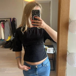 Svart topp med öppen rygg - Svart topp med öppen rygg från Nelly med knyt i ryggen och halvlånga ärmar. Toppens öppna rygg och tighta passform ger en snygg och trendig look. Perfekt att styla med jeans eller kjol för en cool vibe. Endast använd en gång💖💖