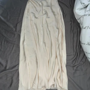Champagnefärgad satinkjol med dragkedja - Supersnygg långkjol i champagnefärgad satin-look. Storlek S (tror jag) och kommer inte ihåg var jag köpte den någonstans. Säljer då den inte kommer till användning