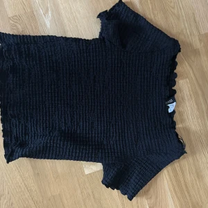 Svart smockad topp från Zara - Svart smockad topp från Zara med korta ärmar och stretchig, ribbad struktur. Toppen har en croppad passform och vågiga kanter vid ärmslut och nederkant. Perfekt för dig som gillar en enkel men trendig look.