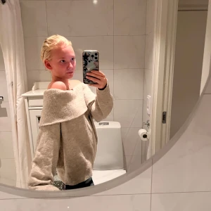 Beige offshoulder stickad tröja - Supermysig beige stickad tröja med bred offshoulder-krage. Tröjan har en loose passform och långa ärmar, perfekt för lager på lager. Enkel att styla till både jeans och kjol. Snygg och chill vibe!