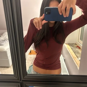 Mörkröd långärmad topp - Säljer en enkel och stilren mörkröd långärmad topp med tight passform. Perfekt att matcha med jeans eller kjol. Materialet känns mjukt och stretchigt, vilket gör den bekväm att bära hela dagen.