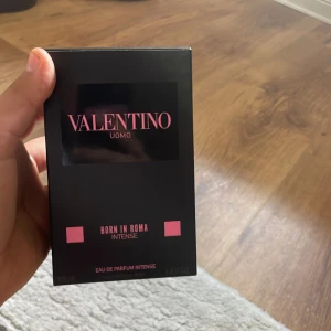 Valentino Uomo Born In Roma Intense - Parfymen Valentino Uomo Born In Roma Intense kommer i en lyxig, mörk glasflaska med nitar och svart kork. Flaskan har en gradient från svart till transparent och rosa detaljer på etiketten. Förpackningen är svart med rosa text och detaljer, vilket ger en modern och edgy känsla. Har kvito 
