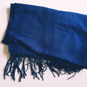 Mörkblå halsduk med fransar - En stilren mörkblå halsduk med långa fransar i ändarna. Halsduken är mjuk och lätt, perfekt att slänga över axlarna för extra värme. Enkel design utan mönster, passar till de flesta outfits och är lätt att matcha.  Helt skick dock noppror