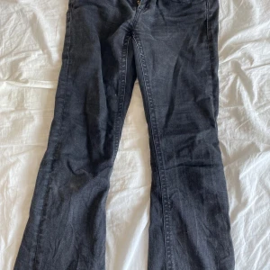 Svarta bootcut jeans Gina Tricot - Snygga svarta jeans från Gina Tricot i bootcut-modell. Jeansen har klassiska fickor bak med lock och knapp, dragkedja framtill och är tillverkade i ett mjukt bomullsmaterial med lite stretch. Perfekta för dig som gillar en retro vibe.