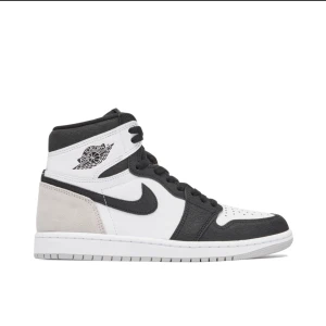 Nike Air Jordan 1 High svart/vit - Nike Air Jordan 1 High i svart, vitt och grått med klassisk vinge-logga på sidan. Skorna har svart swoosh, snörning och hög siluett. Ovandelen är i skinn och mocka, med perforerad tåbox och vit sula. Perfekta för dig som gillar streetwear och ikoniska sneakers.