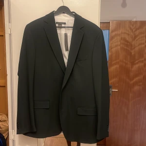 Svart kavaj slim fit stl 56R - Snygg svart kavaj i slim fit med klassisk design och två fickor framtill. Kavajen har slät yta, svarta knappar vid ärmslut och innerficka med satin-detalj. Perfekt för dig som vill ha en stilren och modern look.