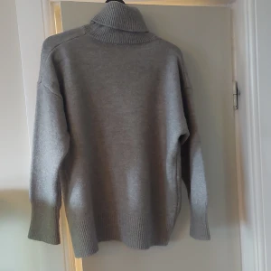 Grå polotröja  - Mysig grå polotröja med hög krage och ribbade muddar. Trökan är perfekt för kyliga dagar. Tillverkad i mjuk ullmix som håller dig varm och bekväm hela dagen. Har klippt bort lappen men har för mig att den är xs-s 
