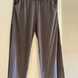 Grå mjukisbyxor från First Class - Mysiga grå mjukisbyxor från First Class med elastisk midja och raka ben. Byxorna har en avslappnad passform och är tillverkade i ett mjukt, lent material som känns skönt mot huden. Perfekta för chill dagar eller när du vill vara bekväm.