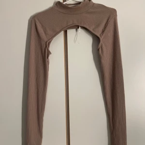 Ribbad brun bolero från NLY Trend - Säljer en ribbad brun bolero från NLY Trend i storlek M. Den har långärmad design, hög hals och är croppad så den täcker bara axlar och armar. Perfekt att slänga över ett linne eller klänning för en trendig layering-look.