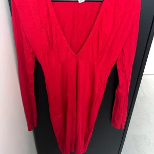 Röd långärmad klänning med v-ringning - En snygg röd klänning med lång ärm och djup v-ringning. Modellen är figurnära och kort, perfekt för dig som gillar en enkel men ändå iögonfallande stil. Tillverkad i mjukt bomullstyg som känns skönt mot huden.