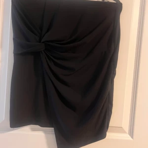 Svart omlottkjol från Gina Tricot - Snygg svart kortkjol från Gina Tricot med omlottkänsla och knytdetalj i sidan. Kjolen har draperad effekt framtill som ger en cool och trendig look. Perfekt för dig som gillar stilrena plagg med en twist.